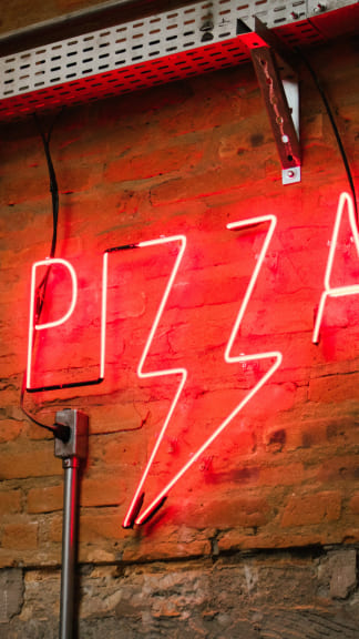 Red neon LED pizza logo light hung up on the brick wall of a pizzeria in the city to attract potential customers