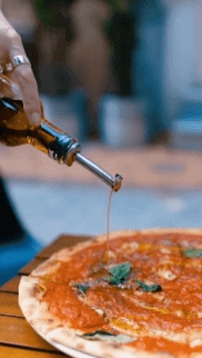User-generated content of olive oil drizzle on pizza with fresh basil used for video marketing